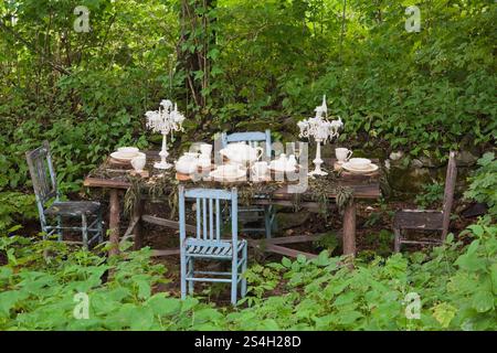 Alter hölzerner Esstisch und blaue Stühle mit hoher Rückenlehne im Schatten-Garten im privaten Garten La Seigneurie de L'Ile d'Orleans im Sommer. Stockfoto