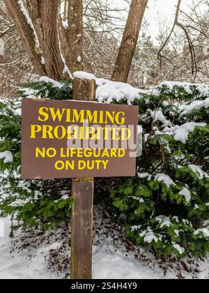 Schild aus verwittertem Holz, Schwimmen verboten kein Rettungsschwimmer im Einsatz, im Winter mit Schnee auf den angrenzenden Büschen, Sträuchern. Stockfoto