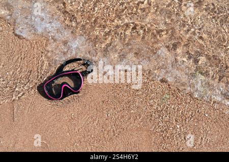 Eine Tauchermaske liegt an einem Sandstrand und wird von Wellen des Wassers gewaschen. Freier Platz für Ihre Materialien. Ein Foto mit hoher Auflösung. Stockfoto