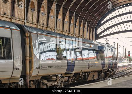 Ein Eisenbahnzug steht unter einem historischen Eisendach aus dem 19. Jahrhundert. Eine Ziegelmauer ist seitlich und ein Signallicht ist in der Ferne. Stockfoto