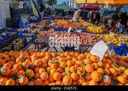 Ein großer Orangenhaufen wird auf einem Markt ausgestellt. Die Orangen sind hoch gestapelt und von anderem Obst und Gemüse umgeben. Der Markt ist geschäftig Stockfoto