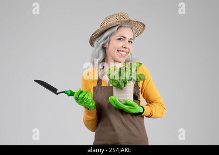Frau mittleren Alters genießt Gartenarbeit mit einer Topfpflanze in den Händen Stockfoto