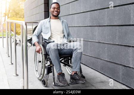 Behindertengerechte Stadt. Positiv beeinträchtigter Afro-Mann im Rollstuhl verlässt das Gebäude im Herbst auf einer Rampe im Freien Stockfoto