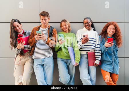 Gruppe verschiedener Teenager, die sich mit Social-Media-Aktivitäten auf Smartphones beschäftigt haben und gemeinsam Momente und Erlebnisse teilen. Fünf multirassische Klassenkameraden benutzen ihre Handys, um im Internet zu surfen. Hochwertige Fotos Stockfoto