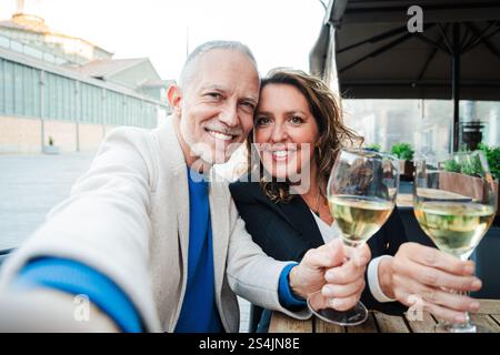 Ein glückliches reifes Paar, das mit einem Glas Weißwein trinkt, einen fröhlichen Moment bei einem romantischen Date genießt, während es ihre Liebe und Verbundenheit auf der Bar-Terrasse während eines Urlaubs feiert. Hochwertige Fotos Stockfoto
