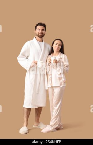 Liebevolles Paar mit Flecken unter den Augen und Tassen Kaffee auf beigefarbenem Hintergrund Stockfoto