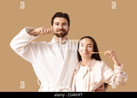 Liebevolles Paar mit Flecken unter den Augen und Zahnbürsten auf beigem Hintergrund Stockfoto