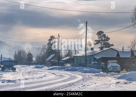 Eine ruhige Winterlandschaft bietet ein friedliches, schneebedecktes Dorf mit gemütlichem Rauch, der aus den Schornsteinen steigt Stockfoto