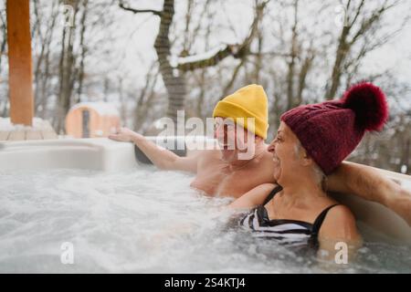 Seniorenpaar baden im Wannen-Whirlpool an kalten Wintertagen. Romantischer Wellness-Kurzurlaub mit Spa am Valentinstag-Wochenende. Stockfoto