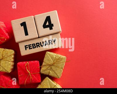 Holzkalender mit dem 14. Februar und kleinen Geschenkboxen auf rotem Hintergrund, die den valentinstag mit Liebe und Zuneigung feiern Stockfoto