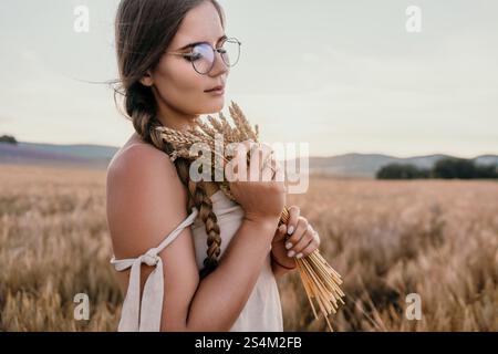 Eine junge Frau auf einem Weizenfeld, die einen Haufen Weizen hält Stockfoto