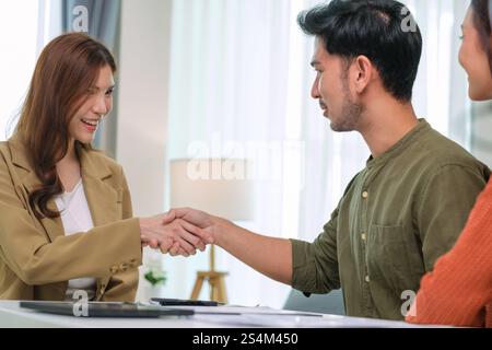 Asiatische Paare handschütteln und unterzeichnen Vertragsfinanzdokumente unter Anleitung eines Beraters zu Hause, Zusammenarbeit und durchdachte Planung für Finanzen Stockfoto