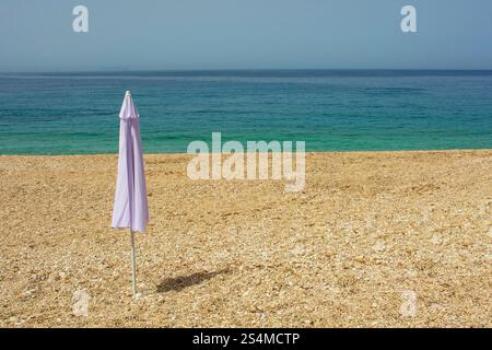 Ein Regenschirm am Prinos Beach am südlichen Ende der Himare Bay an der Küste Südalbaniens, Teil der albanischen Riviera. Morgens im Juni, Frühsommer Stockfoto