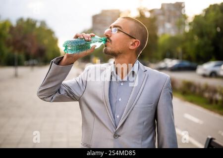 Porträt eines jungen Geschäftsmannes, der auf der Straße steht und Wasser trinkt. Stockfoto