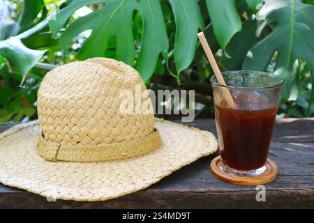 Strohhut mit breiter Krempe und einem Glas gekühlten Eiskaffee auf dem Gartentisch Stockfoto