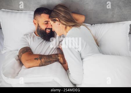 Das junge, glückliche Liebespaar liegt morgens im Bett. Sie sind entspannend und lächeln. Stockfoto