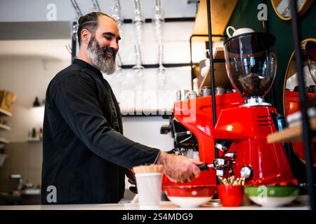 Professioneller Barista in schwarzer Schürze, der im Restaurant arbeitet. Porträt glücklicher Barkeeper, die in seiner Bar Kaffee machen. Stockfoto