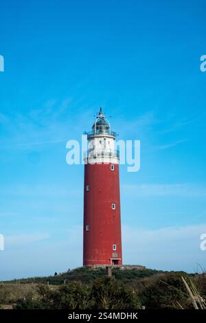 Eierland, de Cocksdorp, Texel, Niederlande, 28. Oktober, 2024, Ein atemberaubendes vertikales Foto zeigt einen roten Leuchtturm vor einem leuchtend blauen Himmel, umgeben von der Natur Stockfoto