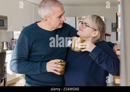 Ein Seniorenpaar, entspannt und glücklich, genießt gemeinsam Kaffee. Sie teilen liebevolle Blicke in einer gemütlichen Küche und spiegeln Liebe und Begleiter wider Stockfoto