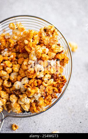 Blick von oben auf eine Glasschale mit knusprigem Karamell-Popcorn, inszeniert auf einem sanften grauen Hintergrund. Stockfoto