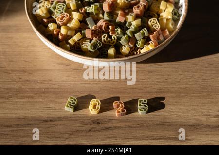 Eine kreative Präsentation zahlenförmiger Pasta, die 2025 klar und deutlich auf einer Holzoberfläche ausdrückt, mit einer Schüssel voller farbenfroher Nudelformen im bac Stockfoto