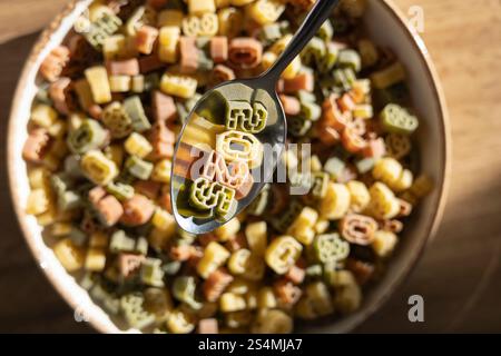Blick von oben auf einen Metalllöffel, der farbenfrohe zahlenförmige Pasta aus einer Schüssel hebt und deutlich die Zahlen 2025 zeigt, die das neue Jahr symbolisieren, inmitten einer Variie Stockfoto