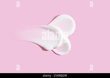 Ein eleganter Abstrich aus weißer Hautpflege-Creme und transparentem Gel auf pastellrosa Hintergrund, der Schönheit und kosmetische Textur symbolisiert. Stockfoto