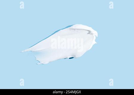 Glatte Textur eines weißen Creme- oder Gelstrichs, isoliert auf einem ruhigen blauen Hintergrund, der Hautpflege- und Schönheitsprodukte darstellt. Stockfoto