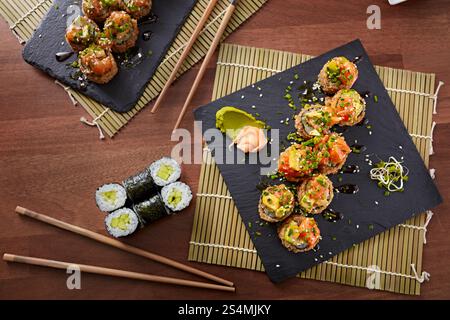 Blick von oben auf eine Vielzahl von Sushi, einschließlich Gurken-Maki und scharfe Thunfischrollen, präsentiert auf einem schwarzen Schiefer, begleitet von Ingwer, Wasabi, Essstäbchen, A Stockfoto