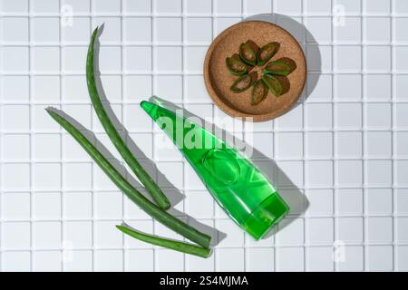Aloe Vera-Blätter und ein Behälter mit Aloe-Gel auf weißen Badezimmerfliesen stehen für natürliche Hautpflege. Stockfoto