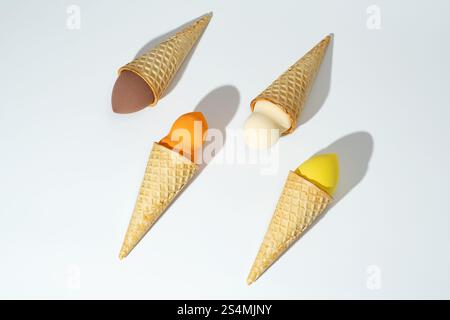 Vier farbenfrohe kosmetische Schwämme, die kreativ in Waffelkegeln angeordnet sind und an Eiskugeln erinnern, vor weißem Hintergrund verspielt und phantasievoll sein Stockfoto