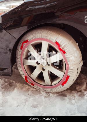 Eine Nahaufnahme eines mit einer roten Schneekette ausgestatteten Fahrzeugrads, die teilweise mit Schnee bedeckt ist und die Winterbedingungen im Stadtverkehr verdeutlicht. Stockfoto