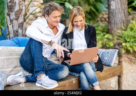 Ein Paar arbeitet gemeinsam an einem Laptop in seinem gemütlichen Home-Office im Freien, umgeben von üppigem Grün, konzentriert und engagiert und genießt das flexible Stockfoto