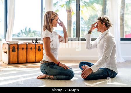 Ein Mann und eine Frau meditieren in einem hell beleuchteten Raum und nutzen alternative Arbeitsstrategien. Die Frau schließt ihre Augen mit Fingern auf den Schläfen, während die Ma Stockfoto