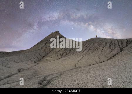 Eine nicht wiedererkennbare Einzelfigur steht auf einem zerklüfteten Hügel unter dem Sternenhimmel der Milchstraße in der Wüste Utah, USA, und zeigt die Weite der Uni Stockfoto