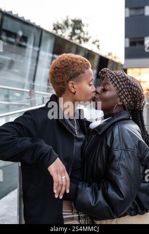 Ein liebevolles multiethnisches LGBT-Paar teilt sich einen zärtlichen Kuss in einer urbanen Umgebung. Sie sind stilvoll gekleidet und strahlen Wärme und Zuneigung aus. Die Szene Captu Stockfoto