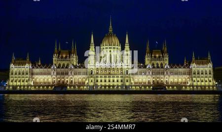Das ungarische Parlamentsgebäude, beleuchtet bei Nacht, spiegelt seine Pracht auf dem Wasser der Donau wider. Stockfoto