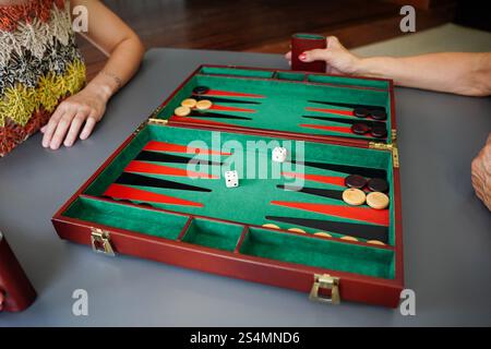 Auf einem lebhaften Brett spielt die Familie ein strategisches Backgammon-Spiel. Die Szene fängt rollende Würfel und positionierte Schachfiguren ein und schafft so ein klassisches Freizeit-M Stockfoto