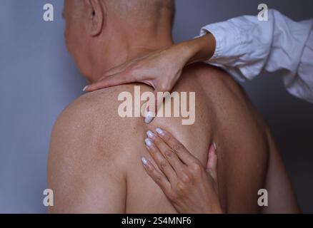 Nahaufnahme eines älteren Mannes, der eine sanfte Massage auf der Schulter erhält und sich auf Entspannung und Wohlbefinden konzentriert. Das Bild fängt das wohltuende Erlebnis ein Stockfoto