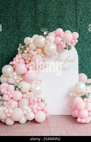 Rosa-weißer Ballonbogen mit „She Said Oui!“ Und florale Akzente. Stockfoto