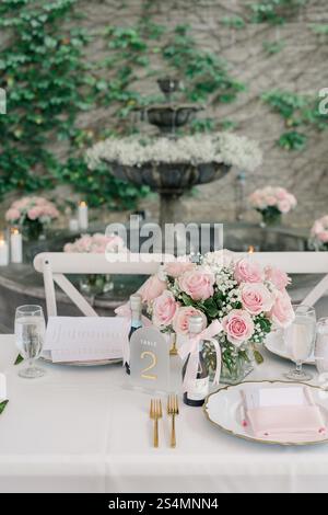 Eleganter Tisch mit rosafarbenen Rosen, goldenen Details und einem Brunnen. Stockfoto