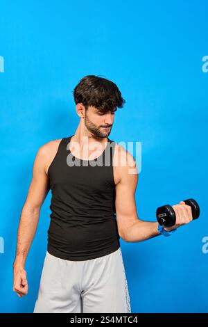 Junger Mann, der Gewichte auf blauem Hintergrund hebt: Konzentrierter Sportler, der Bizepscurl mit Hantel durchführt und Kraft und Fitness gegen vib zeigt Stockfoto