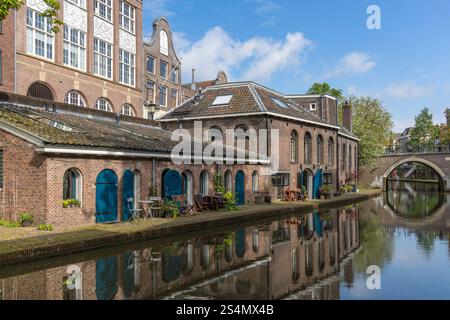 Oudegracht Utrecht mit Ziegelhäusern in der Nähe des Kanals. Eine Brücke mit Fahrrädern, die an den Brücken befestigt sind und sich im Kanalwasser spiegeln. Stockfoto