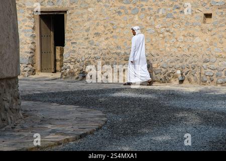 Khasab, Oman - 1. Januar 2025: Ein Mann in traditioneller Kleidung spaziert durch die historische Burg Khasab und zeigt die Mischung aus alter Architektur und Stockfoto