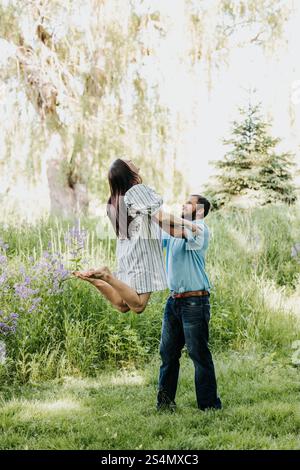 Der Mann hebt die Frau in die Luft, während er lächelt und sie ansieht Stockfoto