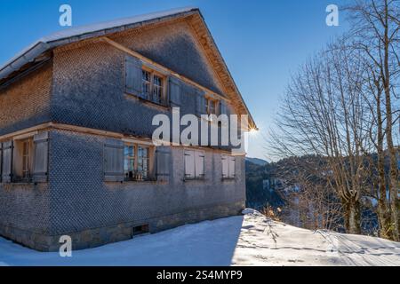Hölzerner alpiner Bauernhof am steilen Hang im Winter, mit Schnee an einem sonnigen Tag, Sonnenstern. Schneelandschaft in österreichischen Bergen, Panoramablick Stockfoto
