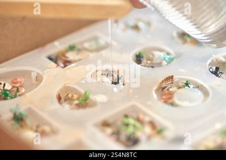 Handgefertigte Schmuckform aus Epoxidharz mit Muscheln und Blumen im künstlerischen Prozess. Stockfoto