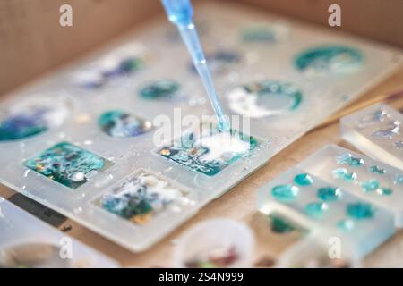 Nahaufnahme des Kunstharzverfahrens mit farbenfrohen Designs und Pipettenapplikation auf geformten Formen. Stockfoto