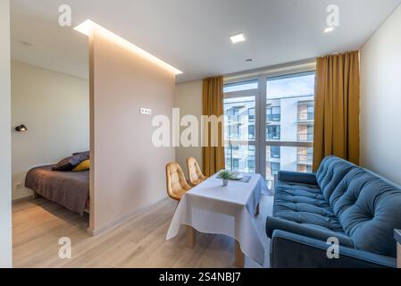 Gemütliches Studio-Apartment mit einem kompakten Wohnbereich mit Sofa, Esstisch und Schlafbereich. Die moderne Innenausstattung umfasst große Fenster, hell Stockfoto