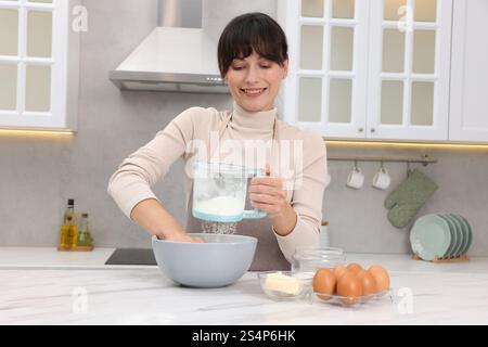 Frau siebt Mehl in eine Schüssel mit Teig an einem weißen Marmortisch Stockfoto